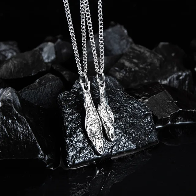 Three silver fish necklaces on dark rocks