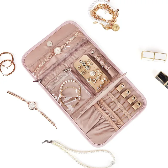 Pink jewelry roll open with loose jewelry arranged around it
