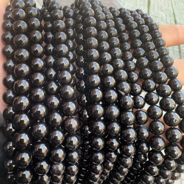 Glossy black agate round bead strands held in a hand for bracelet production