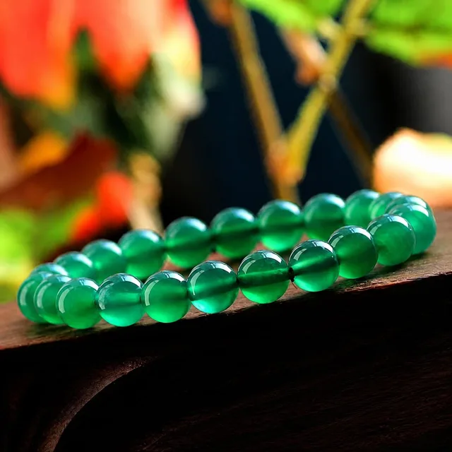 Green agate bead bracelet resting on dark wood with a blurred background