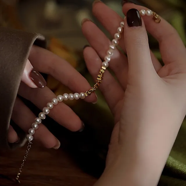 Hand holding a pearl bracelet strung with small gold-tone accent beads and a lobster clasp