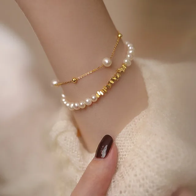 Layered wrist styling with a pearl bracelet and a gold chain bracelet carrying a single freshwater pearl