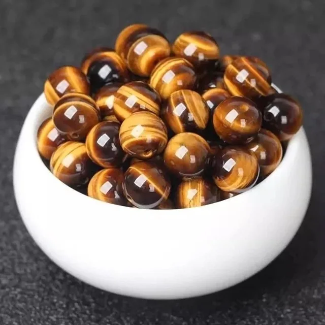 Polished tiger's eye beads in a white bowl showing golden chatoyant banding