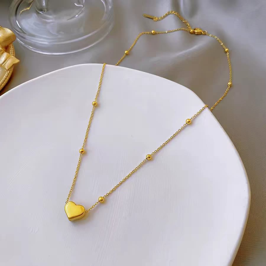 Gold heart pendant on a ball station chain, flat lay